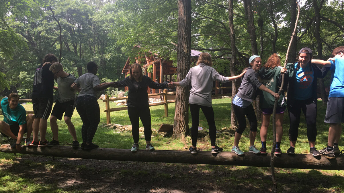 Ten teens linking arms to cross a log