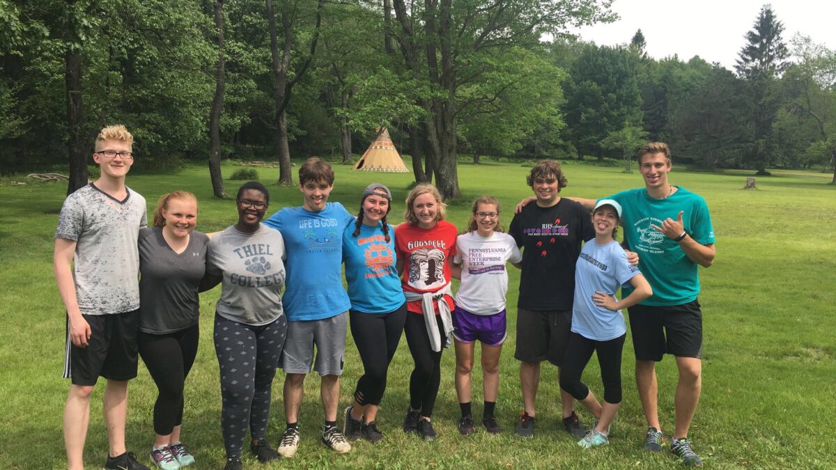 Ten teens smiling and posing in a large green field