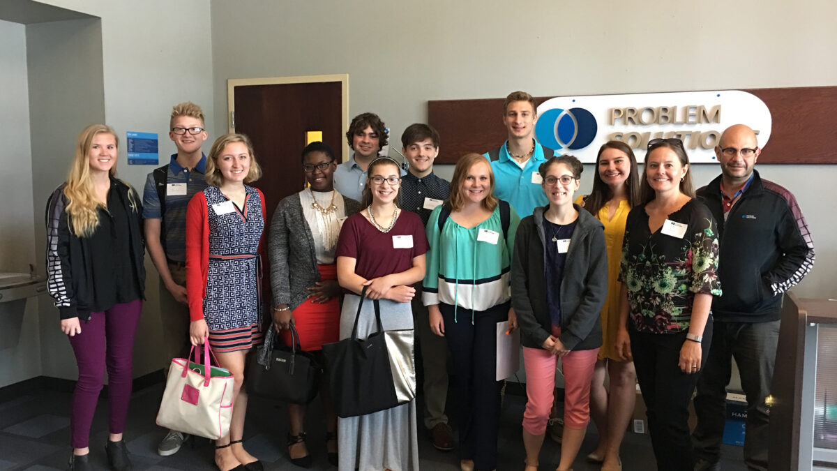 Twelve teens and one adult smiling and posing in an office