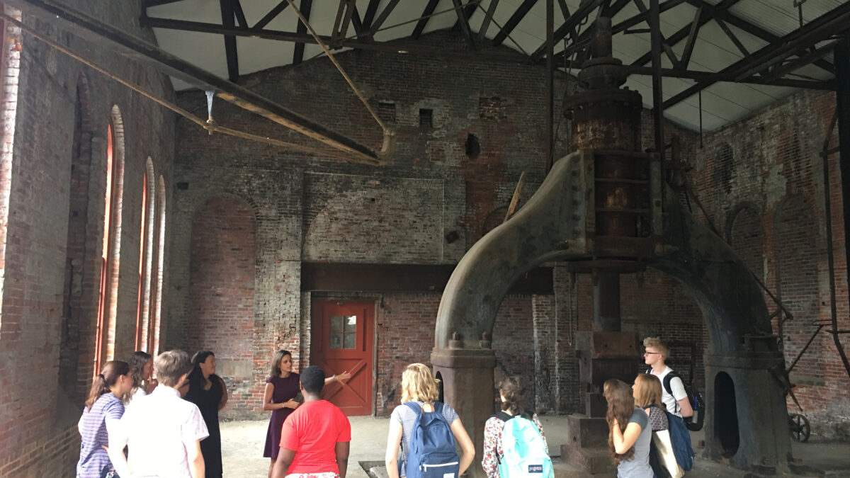 Eleven individuals looking at a large structure in a large brick building