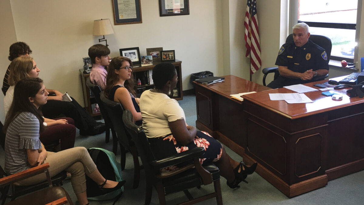Six teens listening to a police officer in an office