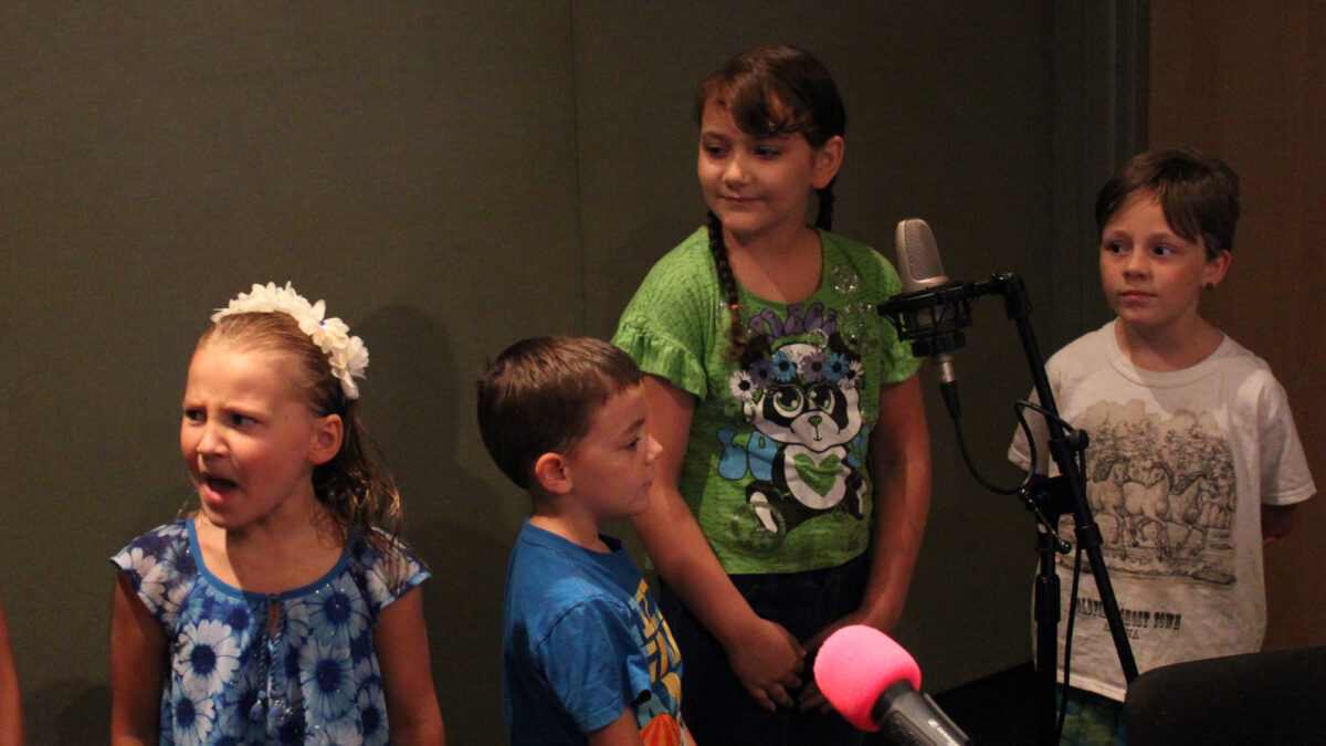 Four youth standing around a microphone in a radio studio