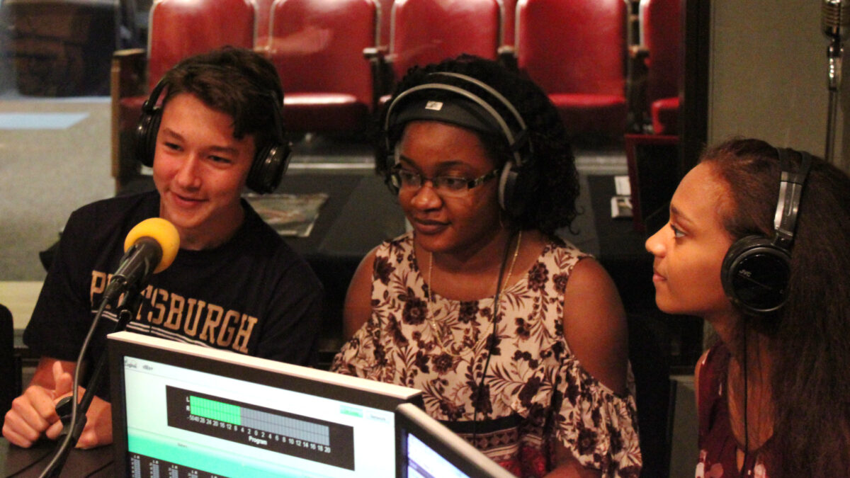 Three teens wearing headphones speaking into microphones in a radio studio