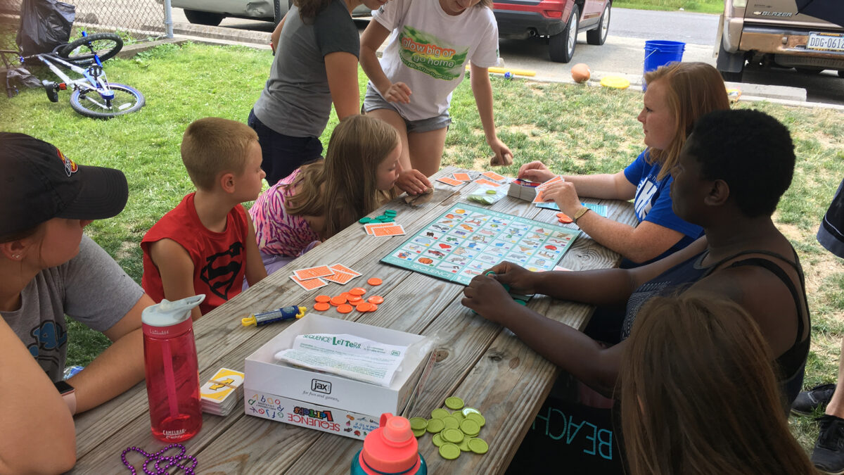 Eight youth gathered around a board game on a picnic table