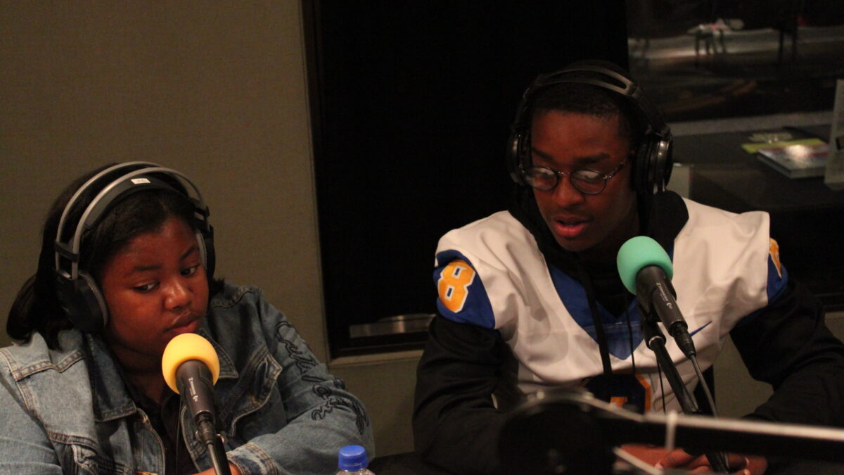 Two youth wearing headphones speaking into microphones in a radio studio
