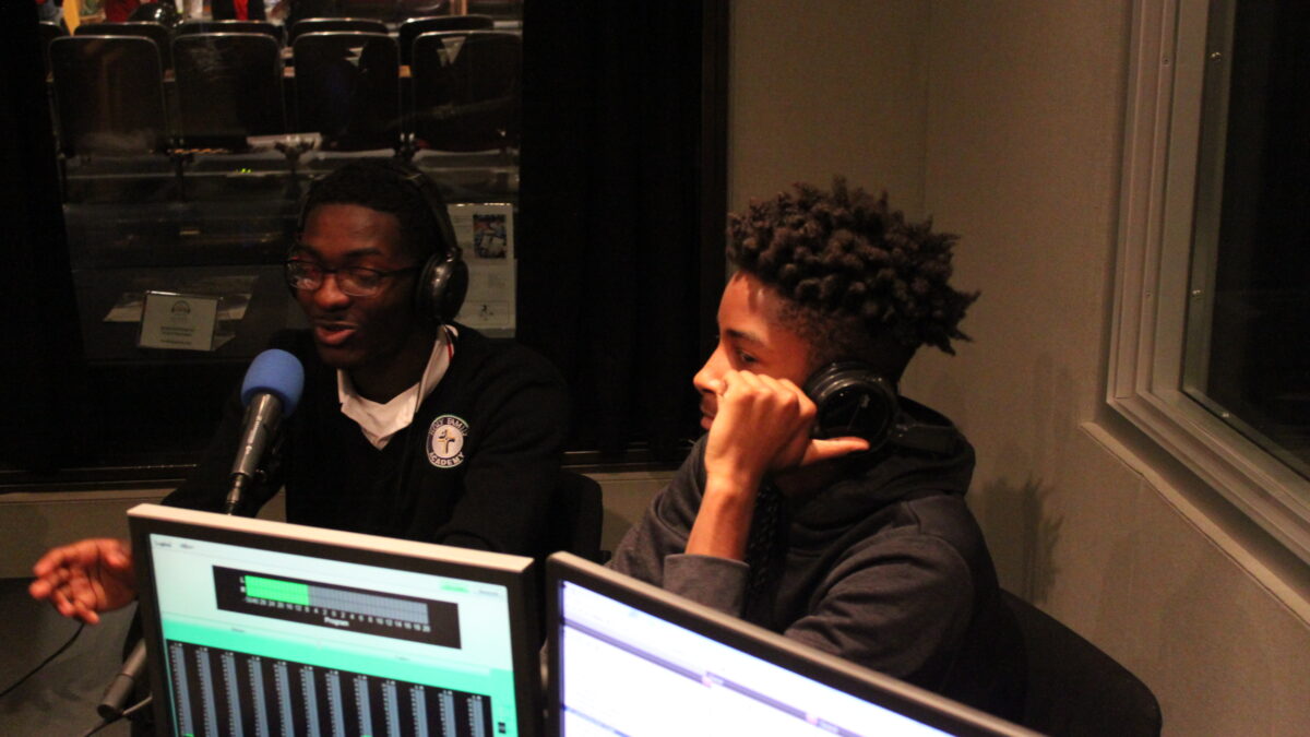 Two youth wearing headphones speaking into microphones in a radio studio