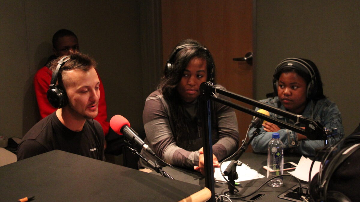 Three youth wearing headphones speaking into microphones in a radio studio