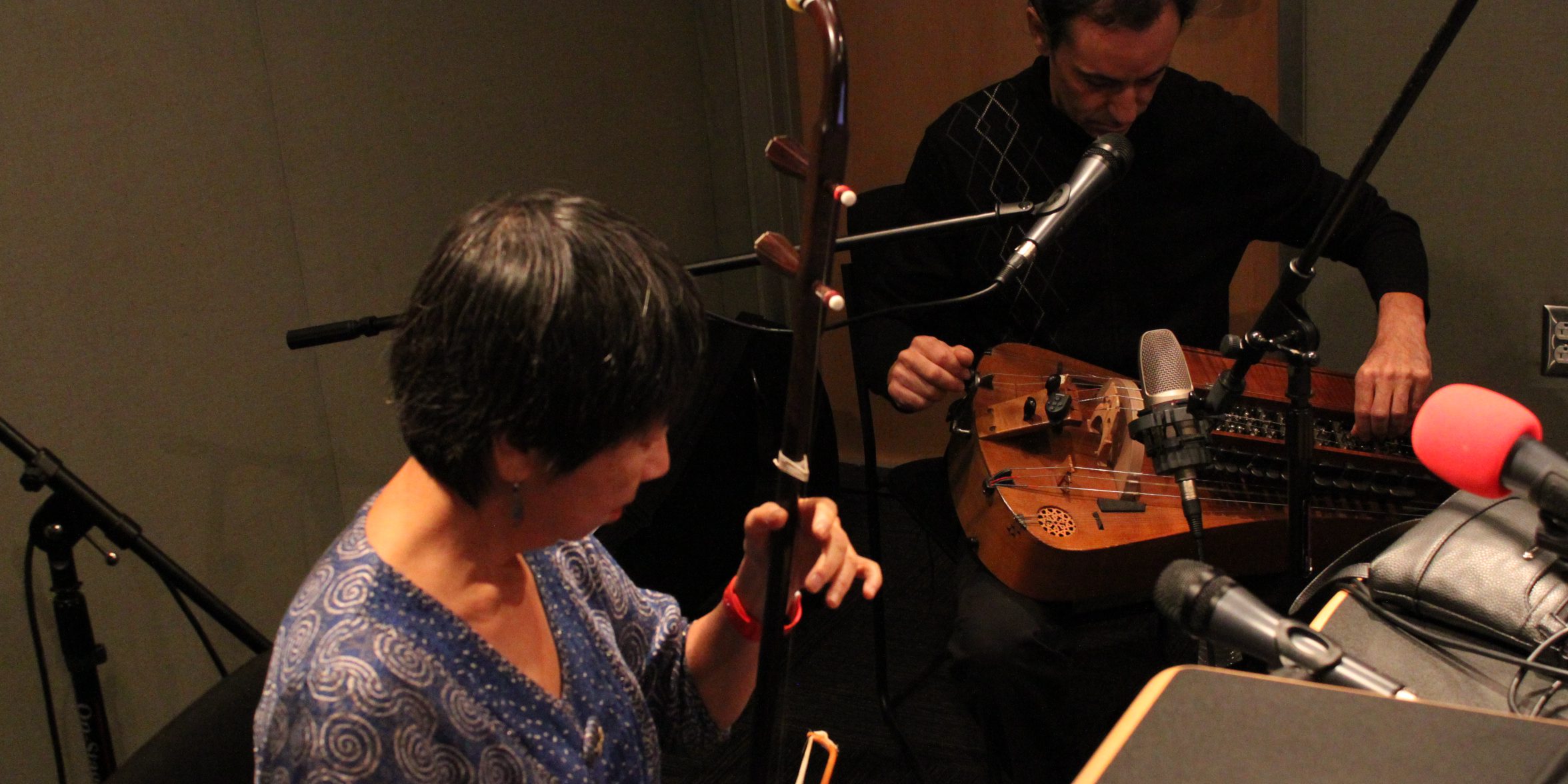 An adult playing a Spanish Hurdy Gurdy and an adult playing a Chinese erhu in a radio studio
