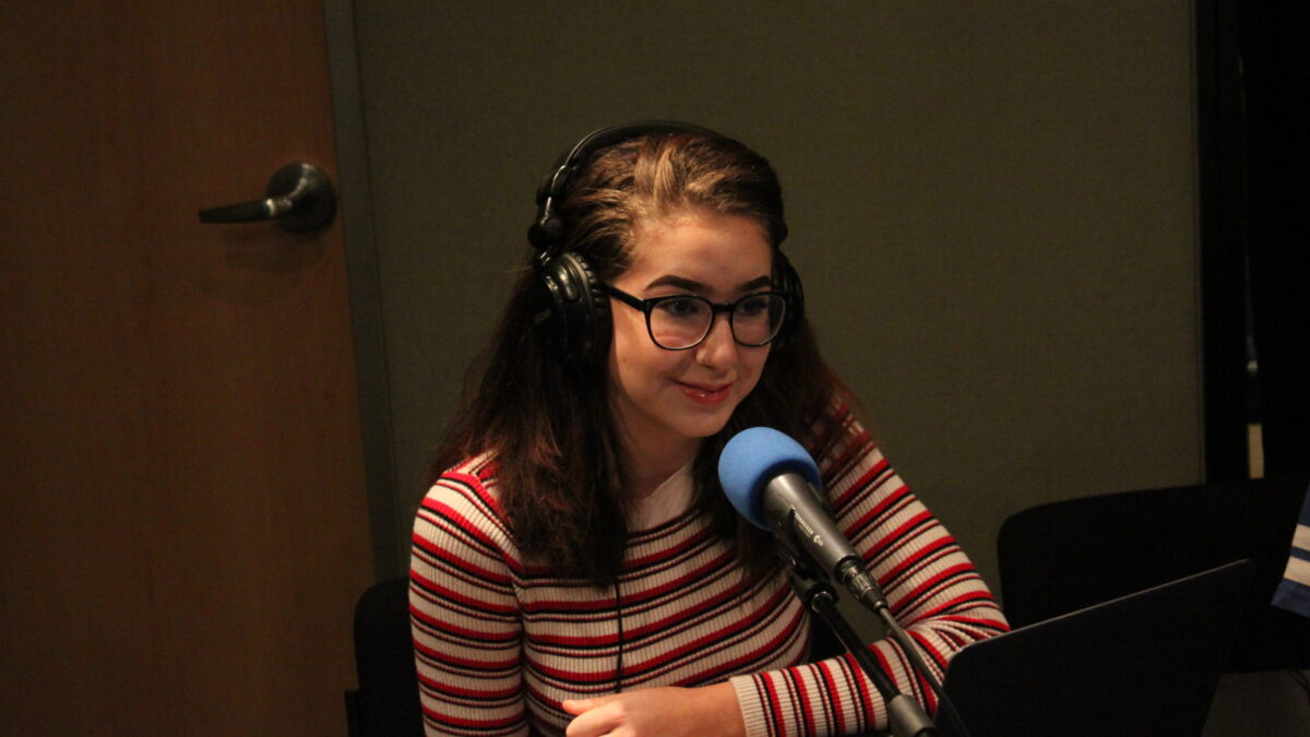 A teen wearing headphones speaking into a microphone in a radio studio