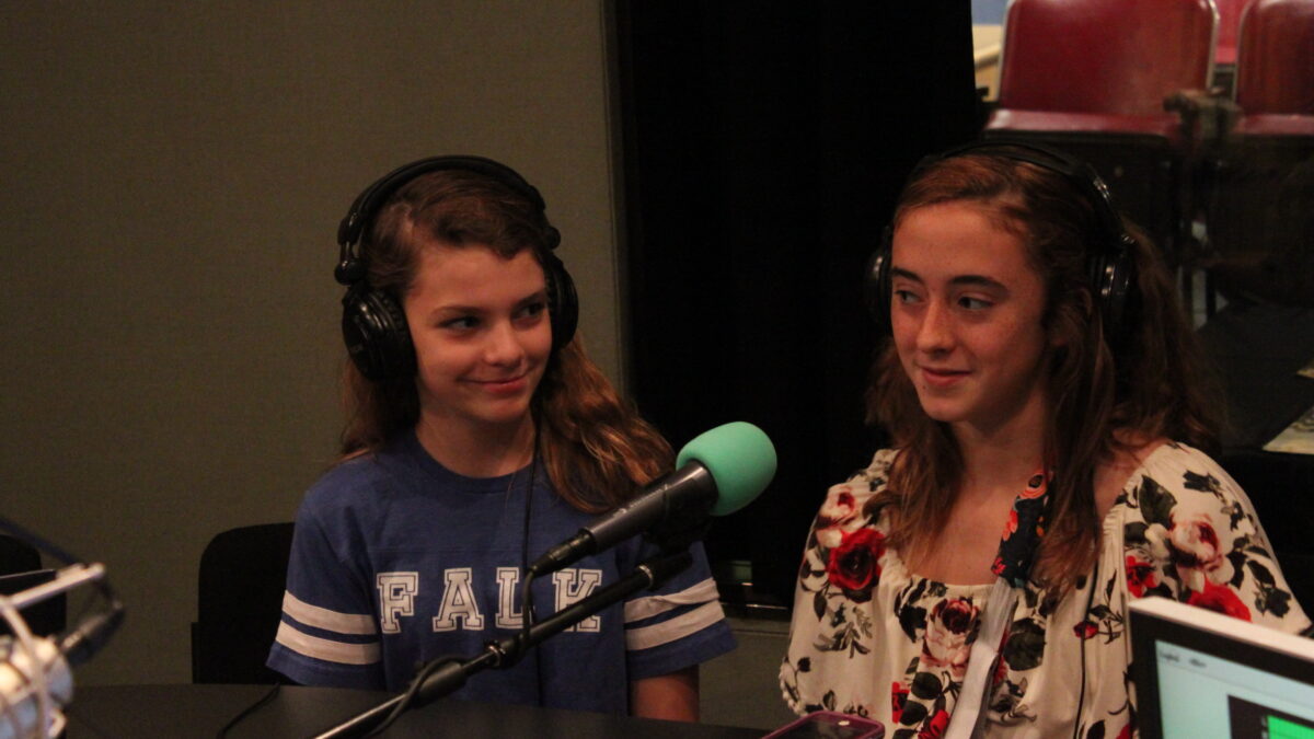 Two teens wearing headphones speaking into microphones in a radio studio