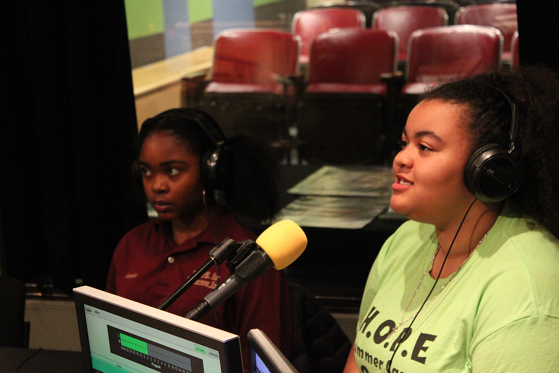 Two youth wearing headphones speaking into microphones in a radio studio