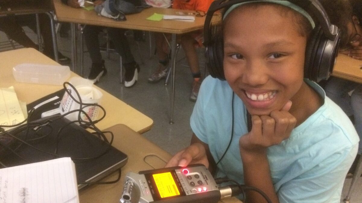 A youth wearing headphones holding a portable recorder in a classroom