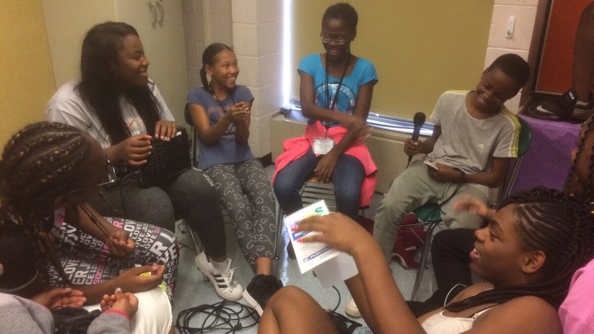 Six youth sitting in a circle having a discussion, one holding a microphone.