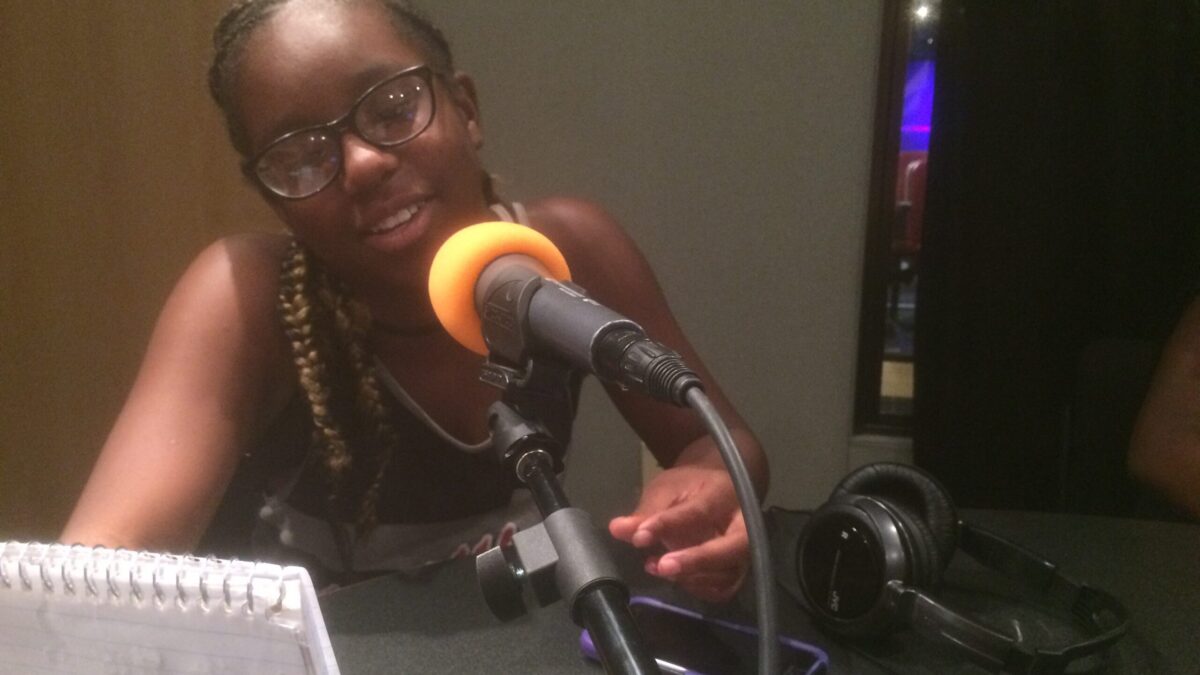A youth reading from a notepad into a microphone in a radio studio
