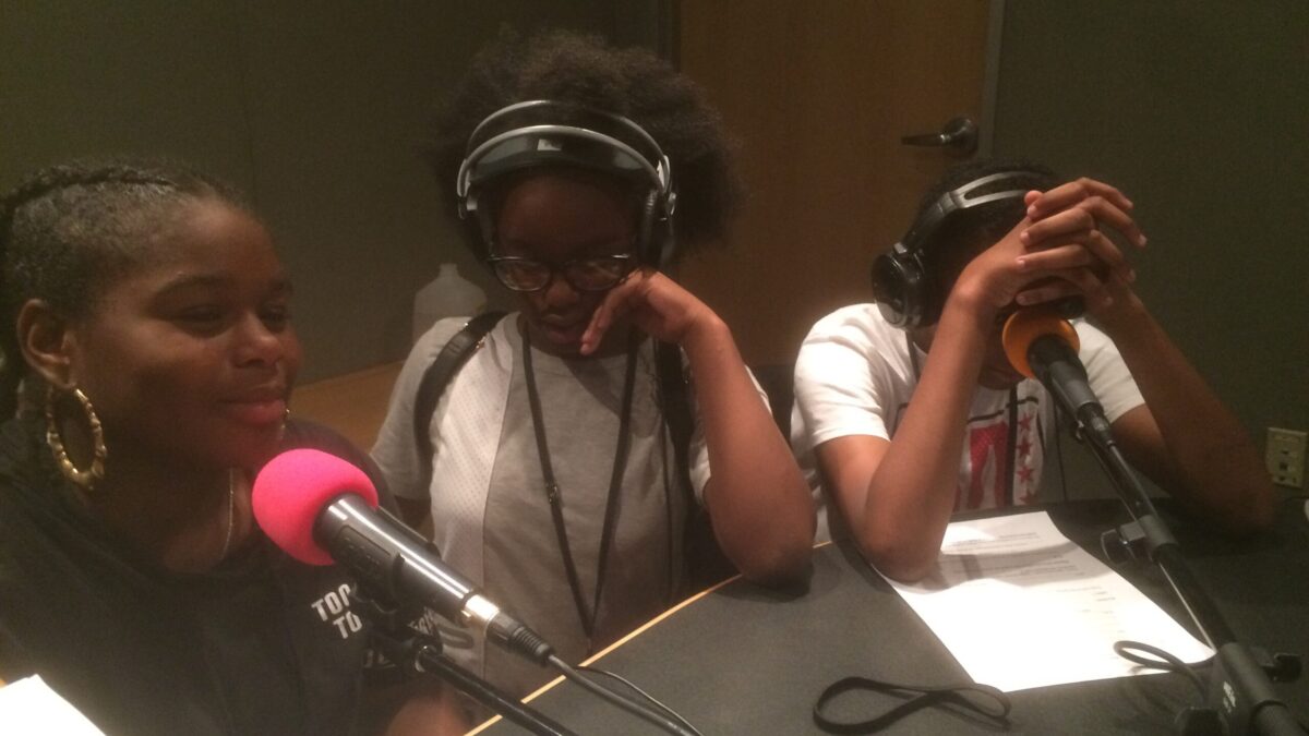 Three youth, two wearing headphones, speaking into microphones in a radio studio