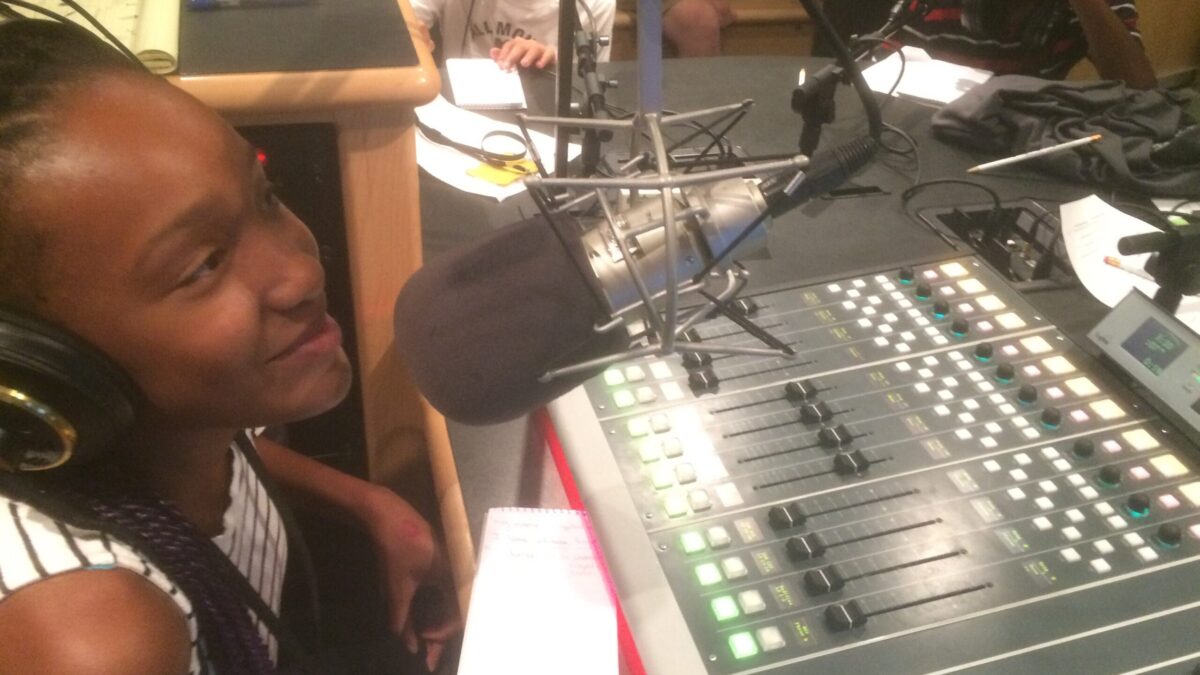 A youth wearing headphones sitting behind a microphone and a mixing board in a radio studio
