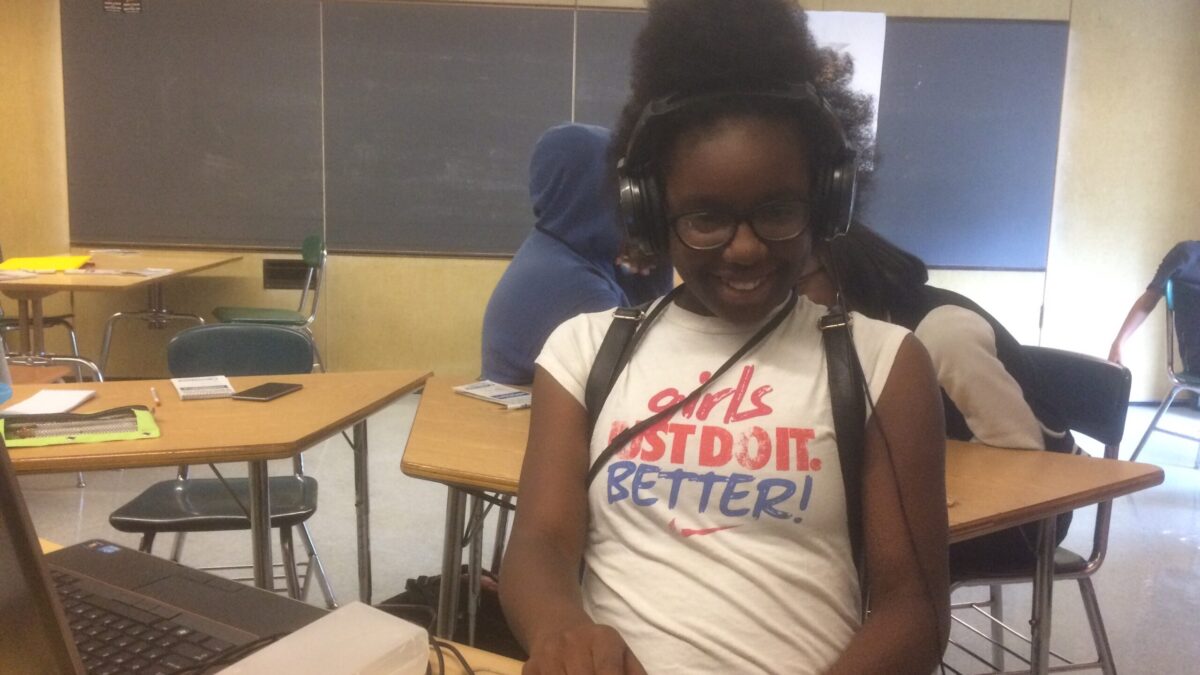 A youth wearing headphones interacting with a portable recorder in a classroom.