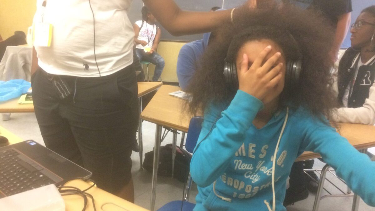 A youth wearing headphones covering their face in a classroom.