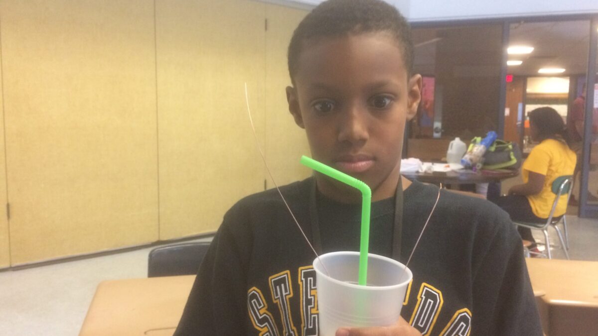 A youth staring at a plastic cup with a light green straw in a classroom