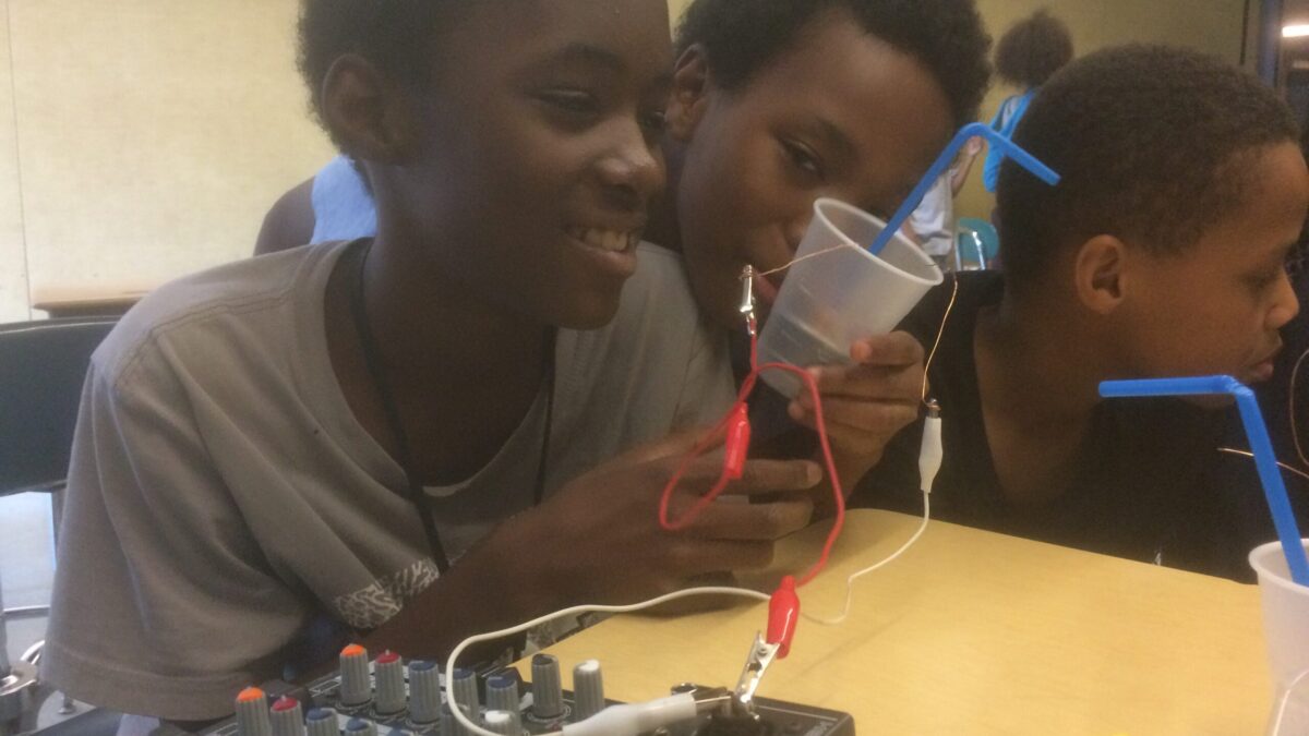 Three youth looking at a plastic cup sitting behind a desk in a classroom