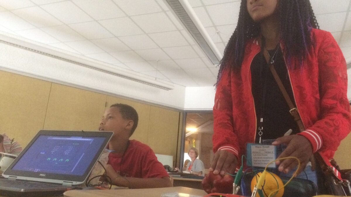 Two youth in a classroom, on interacting with fruit on a classroom desk