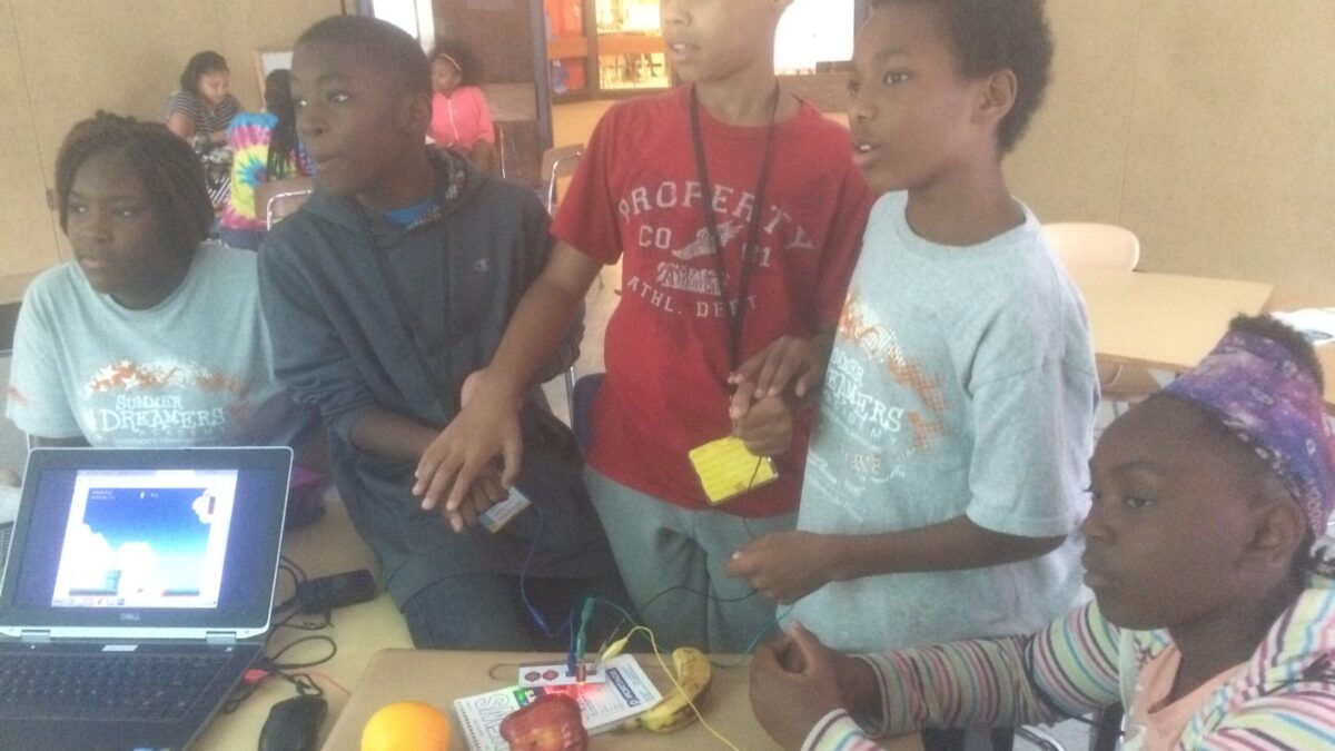 Five youth standing around fruit on a classroom desk