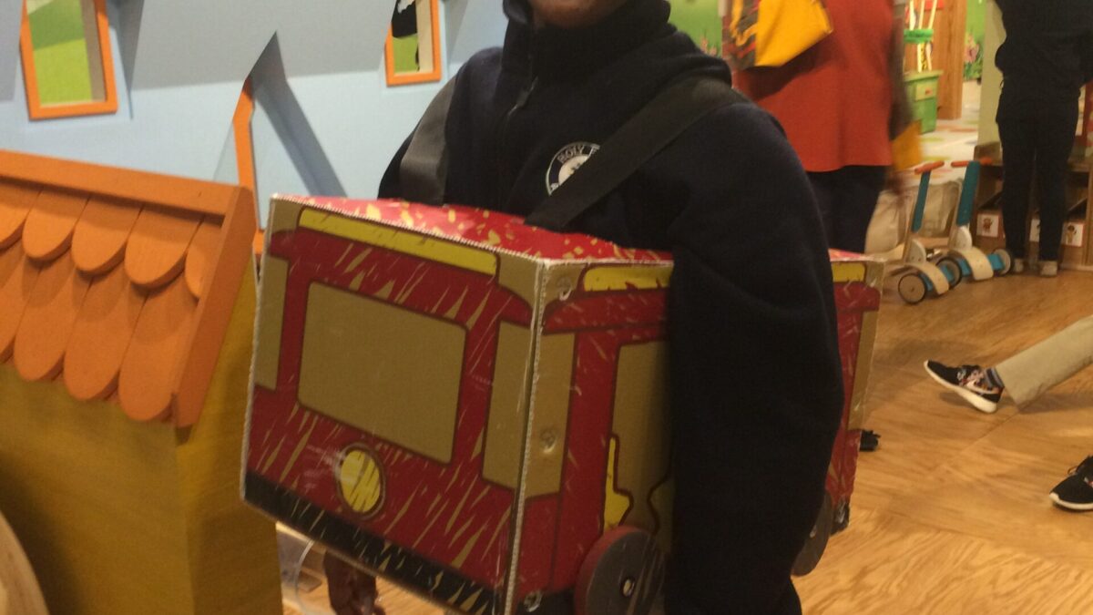 A teen smiling wearing a carboard train car around their waist
