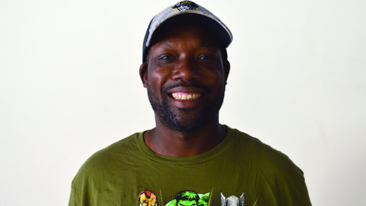An adult wearing a green shirt and a ballcap smiling in profile