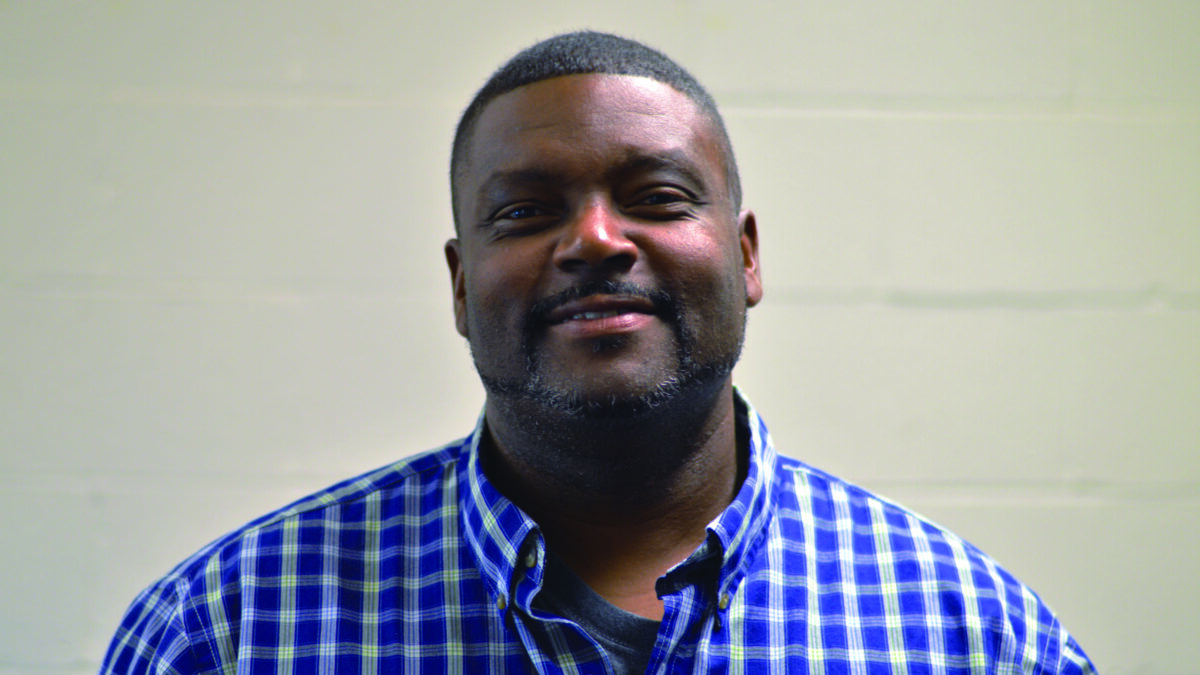 An adult wearing a blue and white checkered shirt posing in profile
