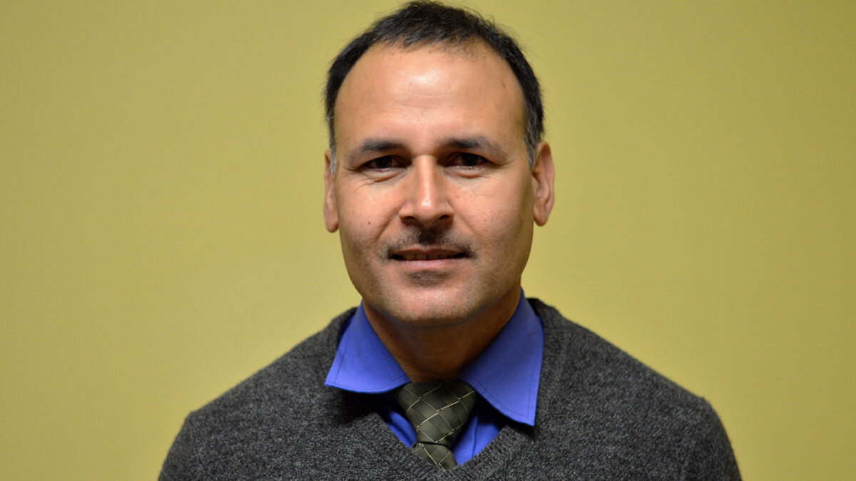 An adult wearing a gray sweater and a blue collared shirt posing in profile