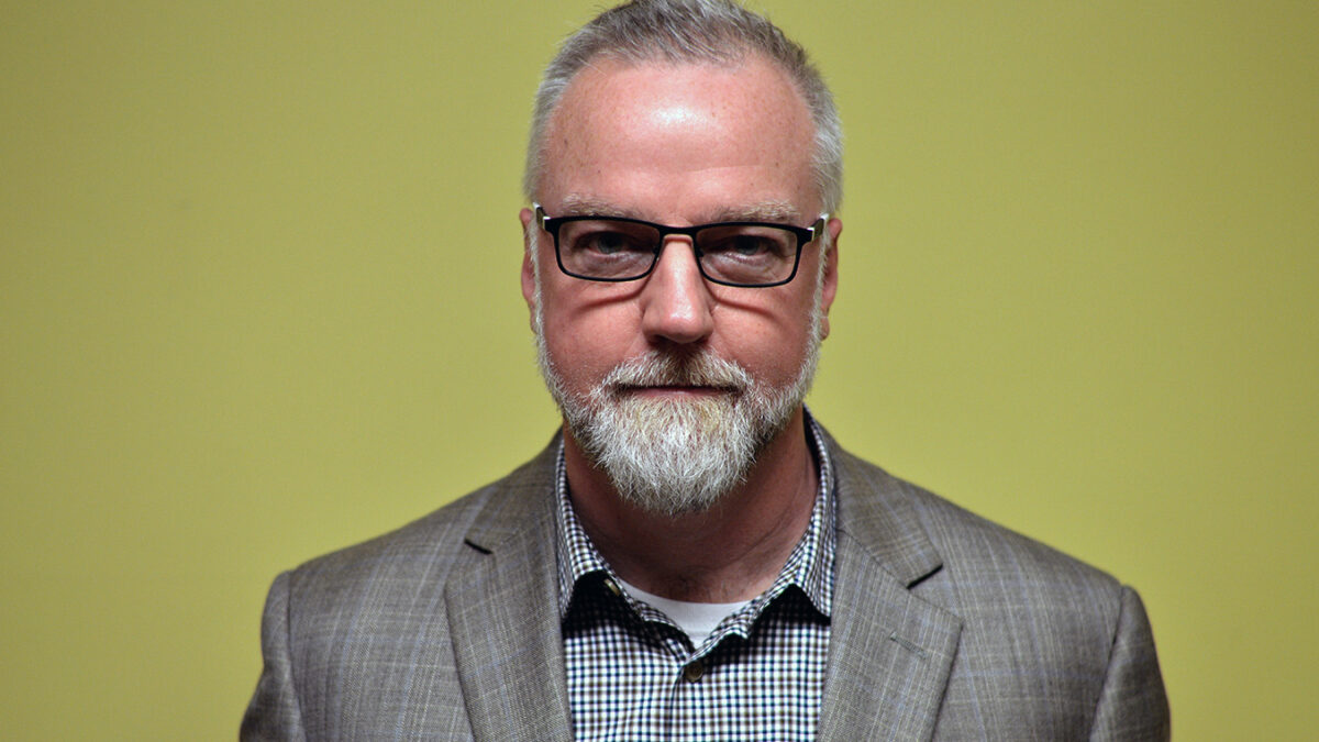 An adult wearing a gray suit jacket and a gray checkered suit posing in profile