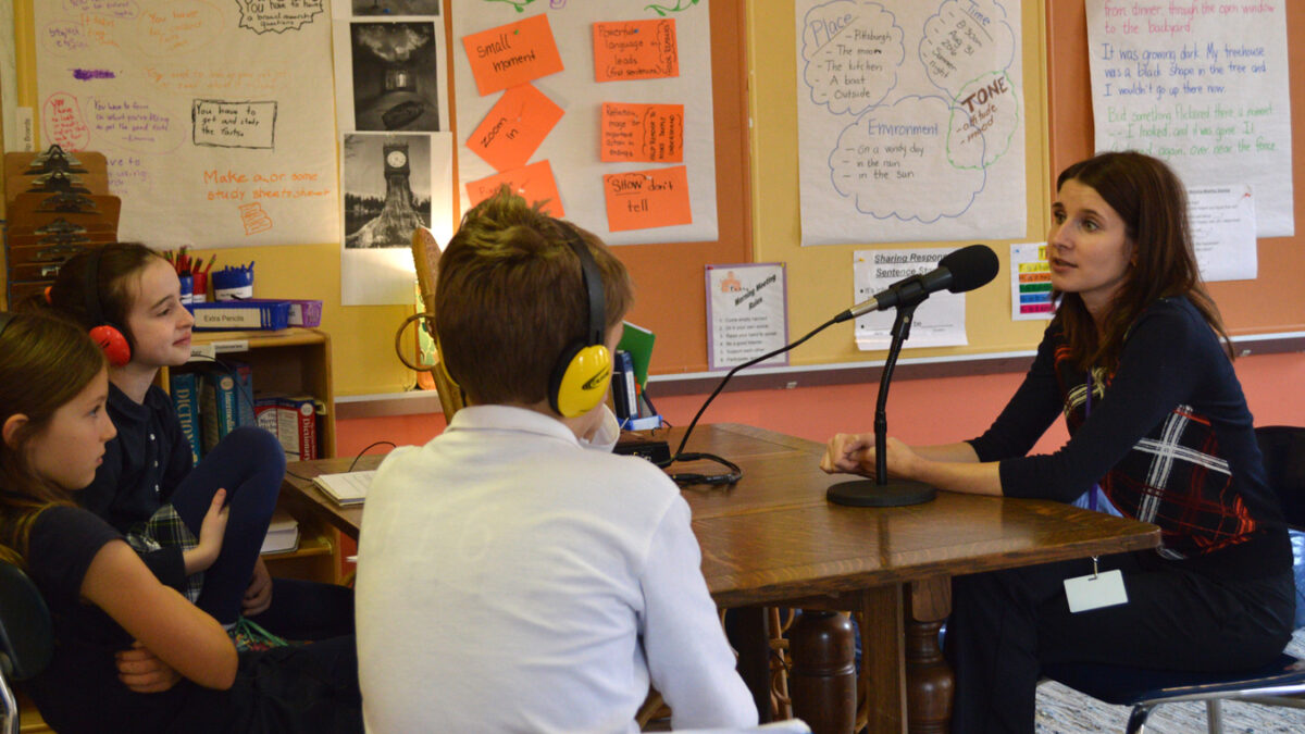 Three youth wearing headphones interviewing an adult speaking into a microphone in a library