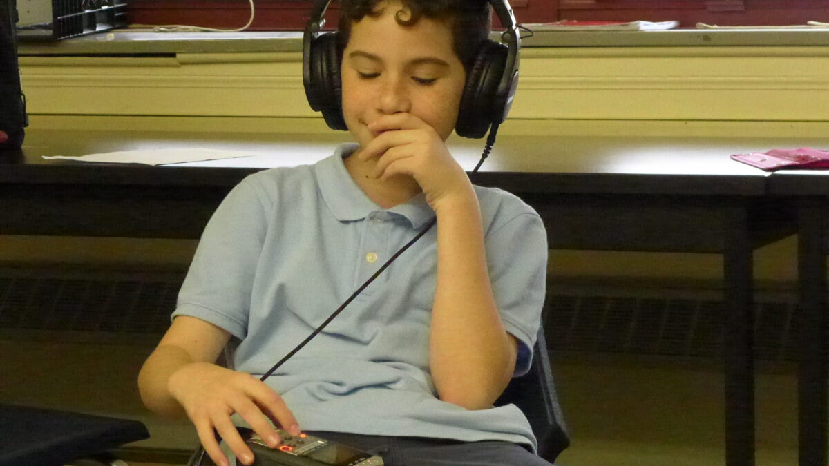 A youth wearing headphones connected to a portable recorder in a classroom