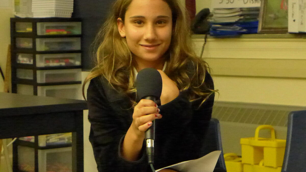 A youth holding a microphone sitting in a classroom