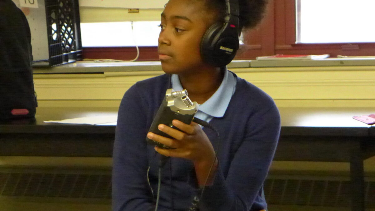 A youth wearing headphones holding a portable recorder in a classroom