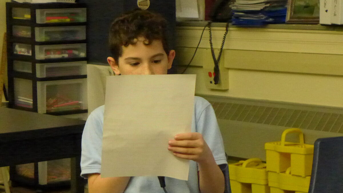 A youth looking at a piece of paper sitting in a classroom