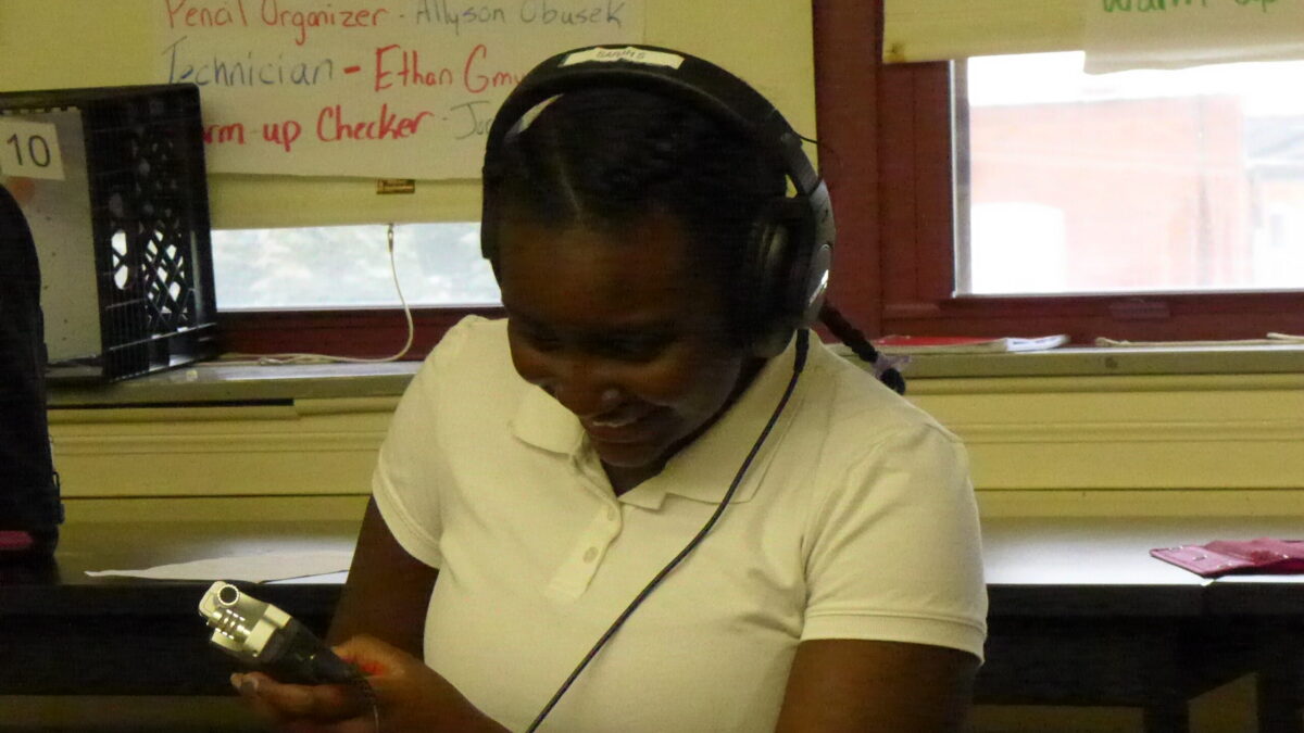 A youth wearing headphones holding a portable recorder sitting in a classroom