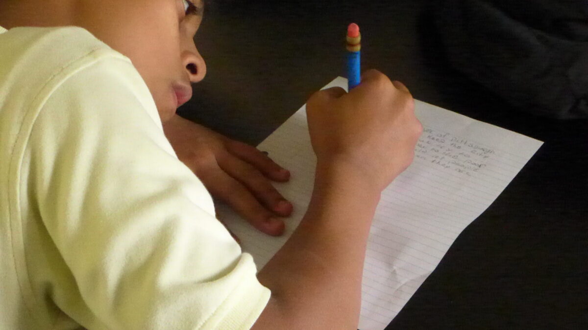 A youth writing into a piece of notebook paper