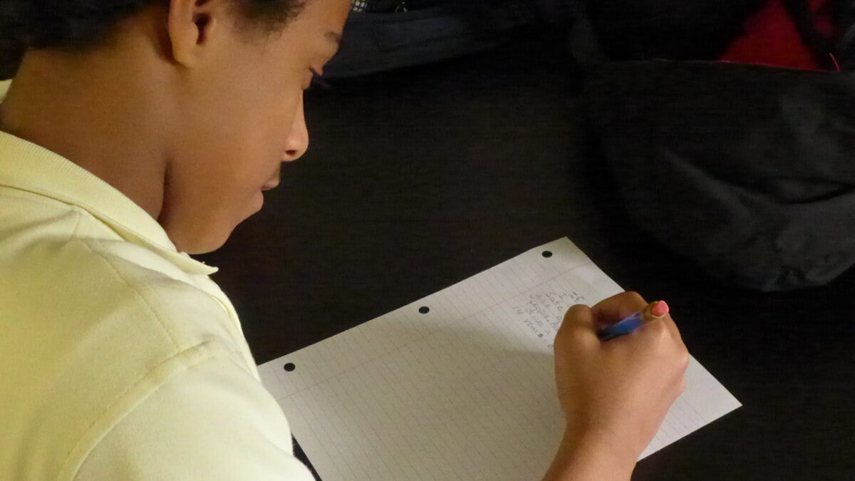 A youth writing into a piece of notebook paper
