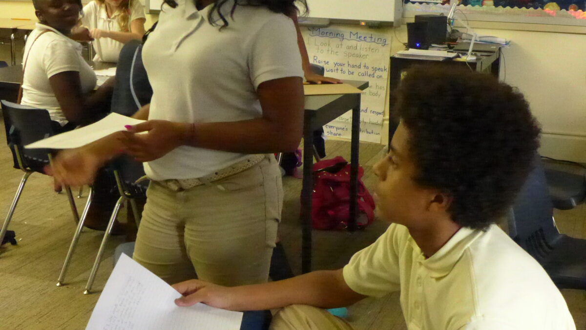Two youth holding pieces of paper in a classroom