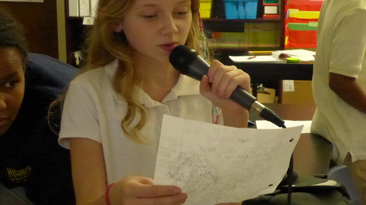 A youth reading a piece of paper speaking into a microphone in a classroom