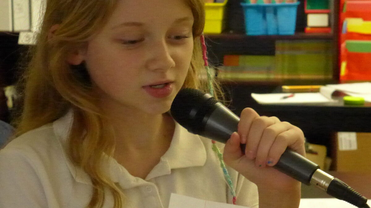 A youth reading a piece of paper speaking into a microphone in a classroom