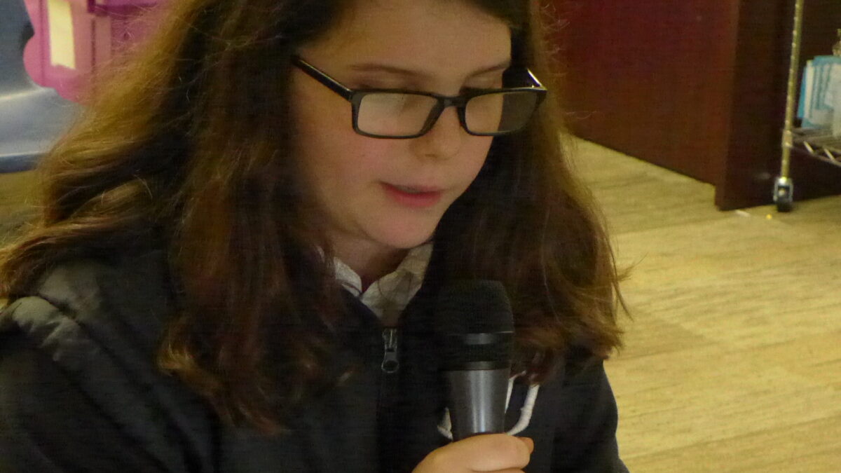 A youth holding and speaking into a microphone in a classroom
