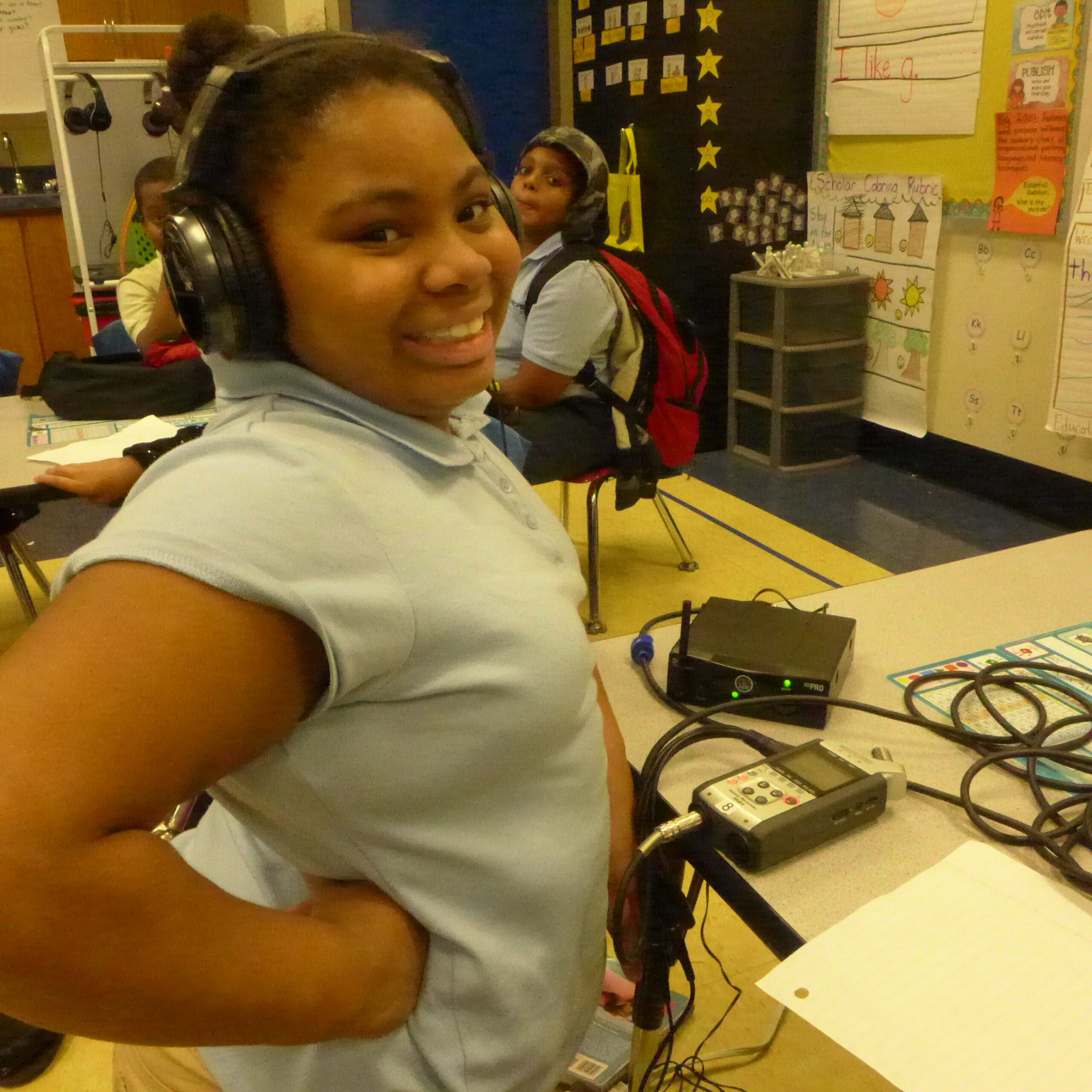 A youth wearing headphones connected to a portable recorder smiling in a classroom