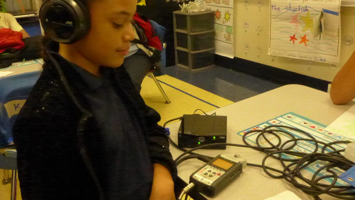 A youth wearing headphones connected to a portable recorder in a classroom