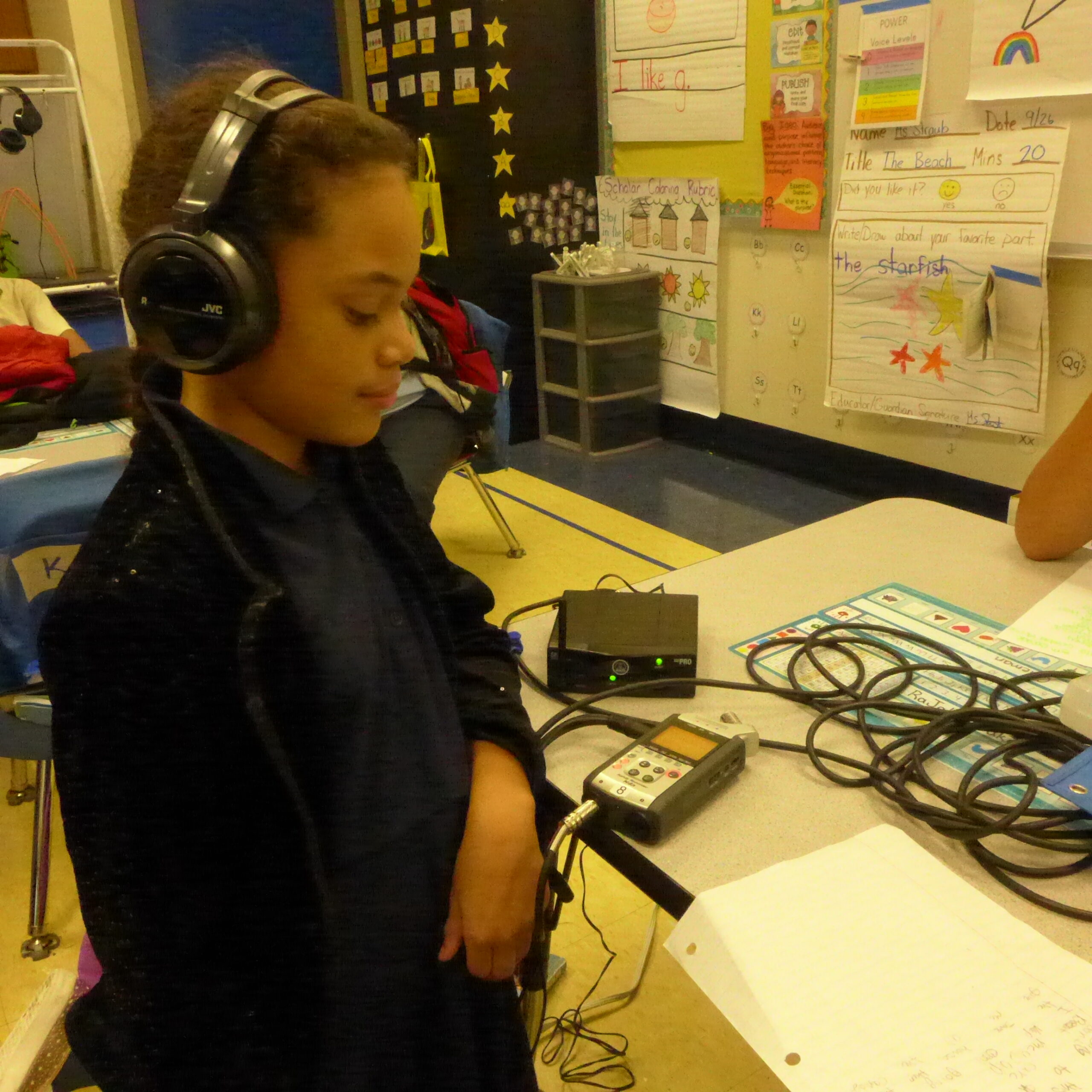 A youth wearing headphones connected to a portable recorder in a classroom