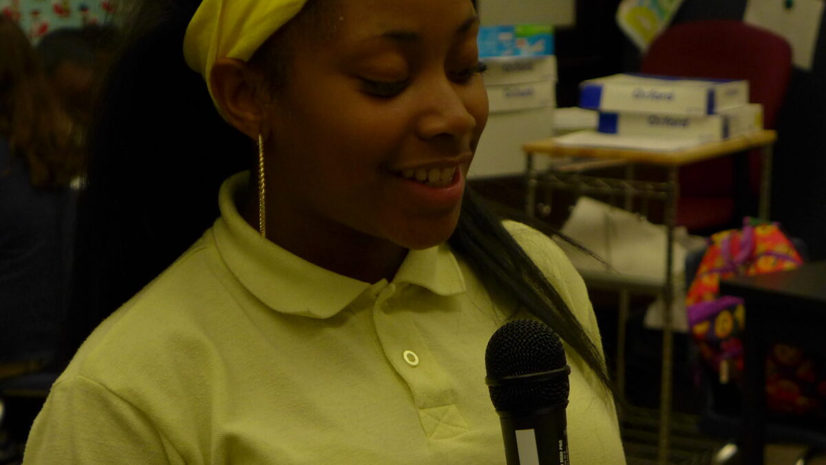 A youth holding and speaking into a microphone in a classroom