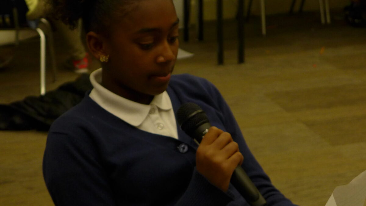 A youth holding a microphone reading a piece of paperin a classroom