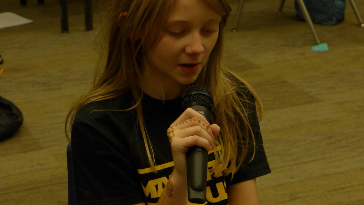 A youth holding a microphone reading a piece of paper in a classroom