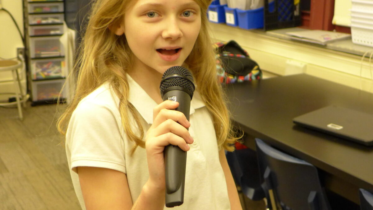 A youth holding and speaking into a microphone in a classroom